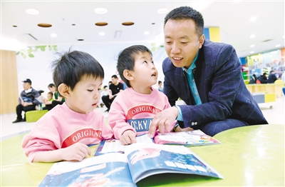 4月21日,一位家长正在内蒙古图书馆教双胞胎宝宝读书识字。