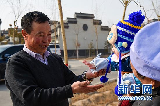 马国权在润丰村的新家门前陪小孙子玩耍(2月18日摄)。新华社发(冯开华 摄)