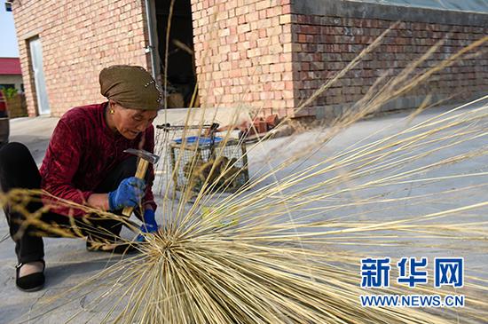 图为李耀梅在对即将扎好的扫帚进行加固。(冯开华 摄)