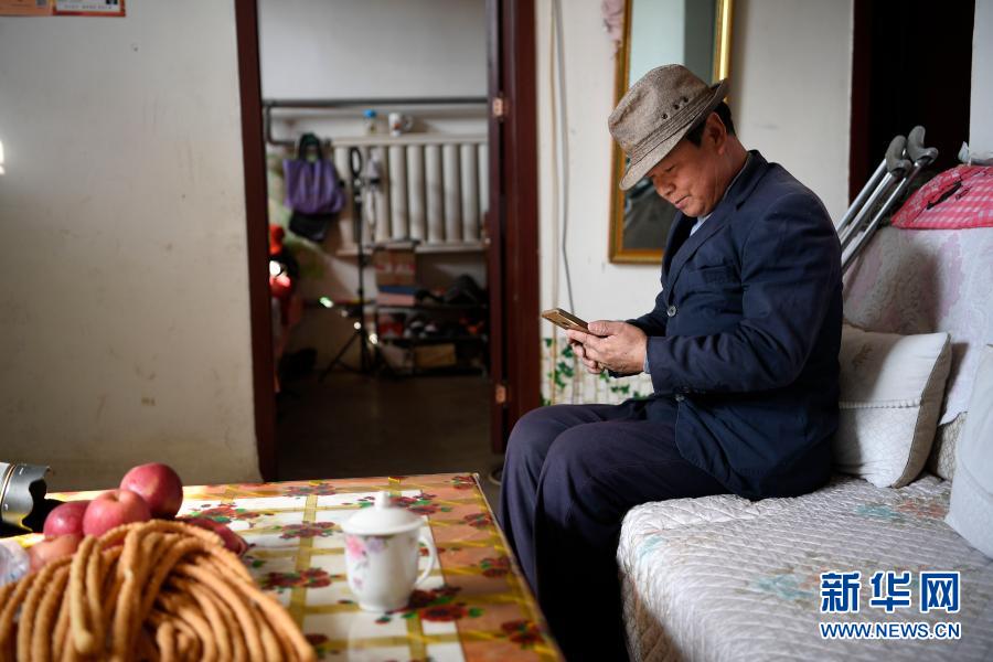 2月11日,张俊明在滨河家园移民村的家中翻看手机,准备网购一些家庭用品。