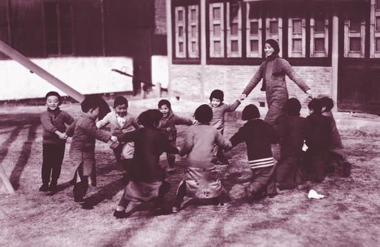 金陵女子文理学院校园即景 1935年12月30日 1935年12月30日，南京金陵女子文理学院的一位年轻的幼教老师带着孩子们在草坪上做游戏。 原载《老照片》第6辑
