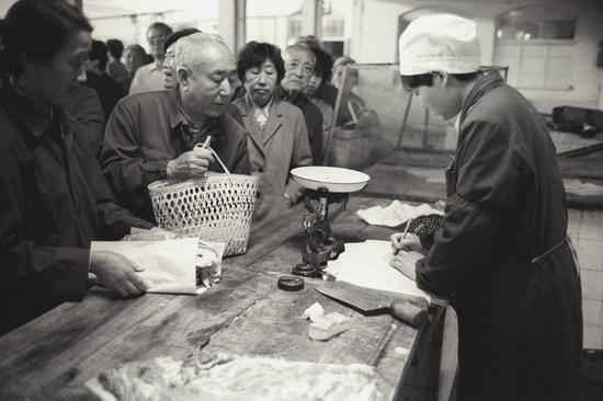 售货员秤完肉，当顾客交了钱和肉票后，在居民购货本上填写购买数量。