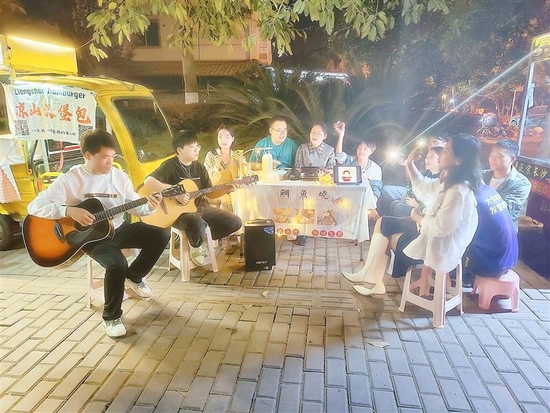 年轻的摊主们收拾好摊位后，围坐在一起弹吉他、哼歌曲。