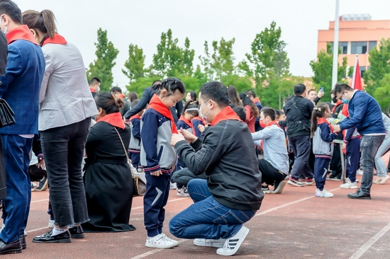 蹲下来,给孩子戴上红领巾