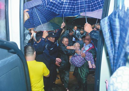 民警和城管队员们用雨伞搭出一条避雨通道,将老人们护送上车。