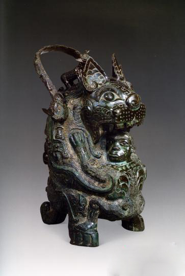 虎卣,商代后期,高35.7厘米,重5.09千克。
虎以后肢及尾部支撑站立,前爪抱持一人。此器具提梁,为运酒器卣的一种。