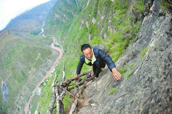 26日,一位村民爬天梯上山,身后陡峭的悬崖让人心惊肉跳。