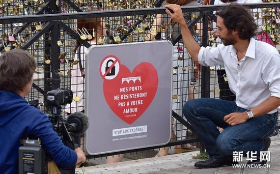 　　8月3日，在法国巴黎，一家电视台记者在新桥上写有“我们的桥承受不了你们的爱情，停止挂锁”的警示牌前做报道。