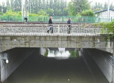 被淹的涵洞内,积水有膝盖深,通行不便的市民们无奈翻过桥上的防护栏横穿铁路。