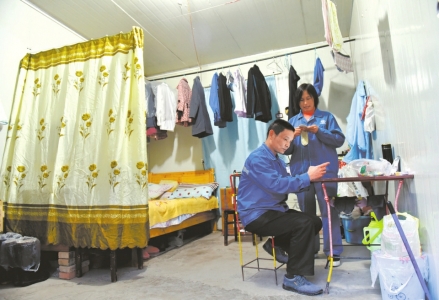 袁志全夫妇住在距离炸药库70米的板房里,下班的闲暇时间,袁志全用手机看小说,妻子在一旁纳鞋垫。