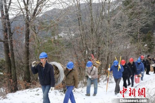 万源市电力抢修人员扛着设备在雪地里前行。 钟欣 摄