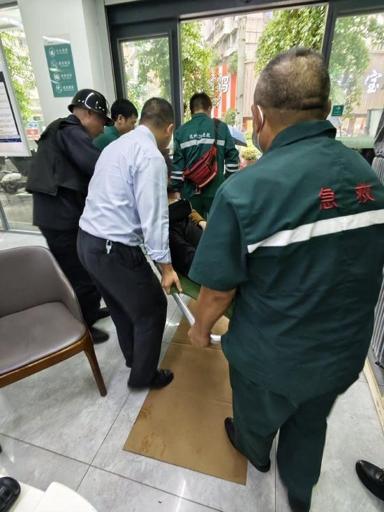 图为农行员工配合医护人员将孙大妈送往救护车