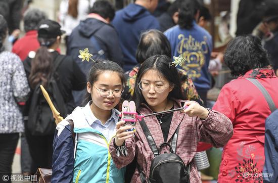 2018年4月14日,济南,两位女孩头戴“风车”头饰在“人海”中玩自拍。
