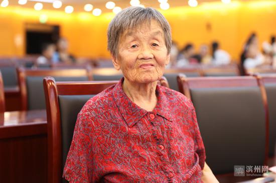 87岁的刘训芝老人在台上领奖，85岁的老伴在台下观看。