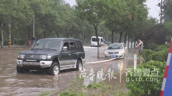 一位女司机害怕水中熄火将车开上辅道上,结果被马路沿石绊住前后不能动,队员大山等两人主动将其车辆拖出。