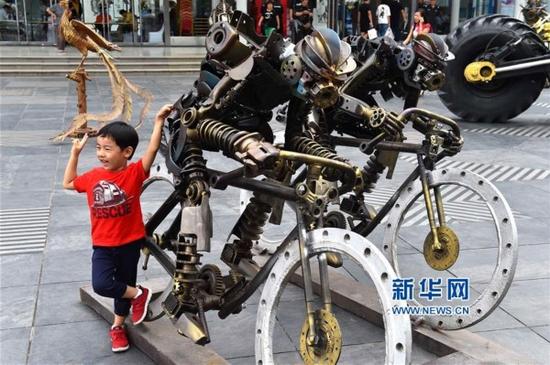 8月26日,一位小朋友在第五屆濟南藝術博覽會上與創意鋼雕合影。新華社記者 郭緒雷 攝