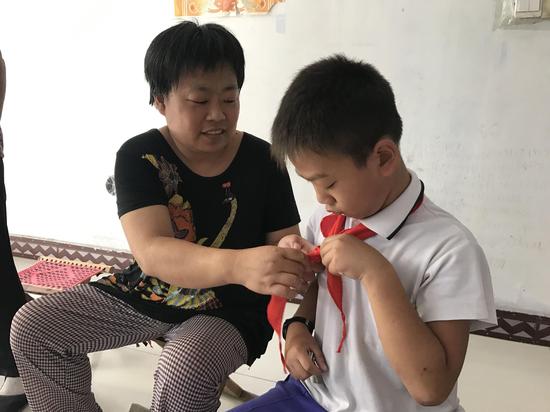 曾接受救助的张玉荣帮儿子整理着红领巾。记者 陈玮 摄