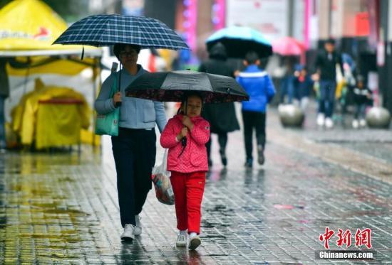 资料图:9月24日,新疆乌鲁木齐市降下秋雨,外出民众打着雨伞快步前行。 中新社记者 刘新 摄