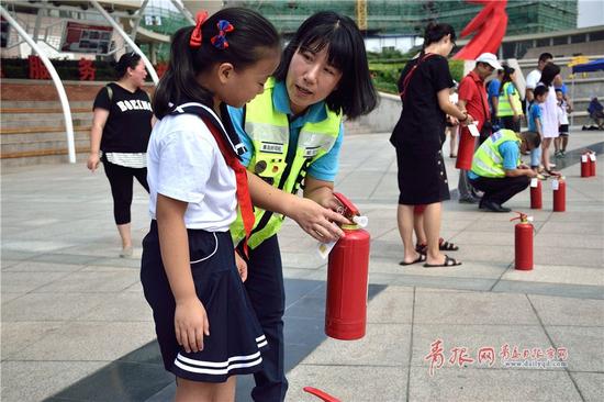 青岛市志愿者广场“应急主题月”活动中，“好司机”志愿者袁嘉秀正在教小学生如何使用灭火器。
