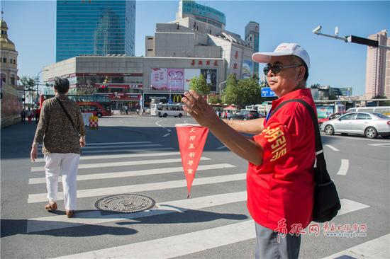 刘长源正在广西路与泰安路交叉口指挥行人过马路。