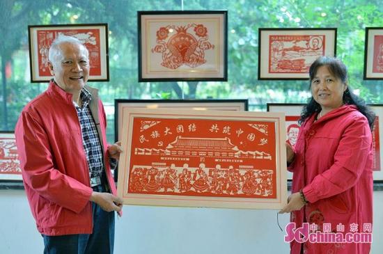 10月12日，在青島市滄口公園鄰里中心，社區居民李德遠夫婦展示自己創作的“民族大團結 共祝中國夢”剪紙作品。