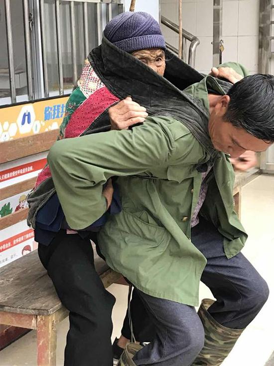 背到村衛(wèi)生室門口,汪克武讓母親坐一張板凳上準(zhǔn)備解繩子。張曉瑜 圖