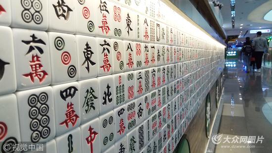 2017年10月23日，在山东济南泉城路一商场内，柜台用密密麻麻的麻将贴成“麻将墙”，吸引众多路人的眼球。