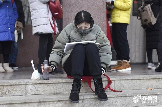 寒冷的冬季，一名女生把自己裹得严严实实，在考点门口外进行最后的复习。