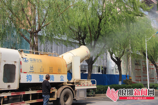 抑尘车对柳树实施高压水雾降絮。