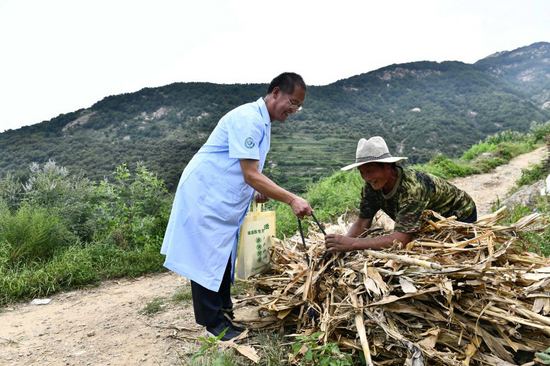 在日照市东港区三庄镇西王家村，乡村医生王远平巡诊途中给正在干活的村民搭把手（8月15日摄）。