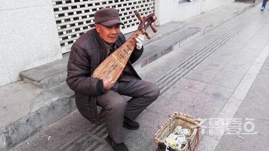 （文化东路山师对面的马路上，一位70岁左右的老人手拉木质柳琴弹奏着小曲）