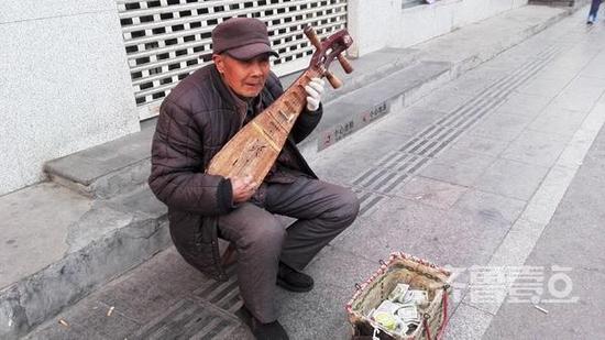 (文化東路山師對(duì)面的馬路上,一位70歲左右的老人手拉木質(zhì)柳琴彈奏著小曲)