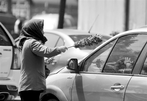 在文化西路和趵突泉南路路口，一名乞讨者用鸡毛掸子为等待红灯的车辆“清理”灰尘
