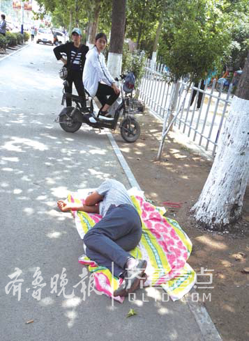 在菏泽牡丹实验中学考场，一位陪考家长躺在树荫下睡午觉。