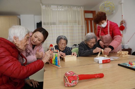 图说：五里桥街道综合为老服务中心内，护工正在陪老人们玩益智游戏