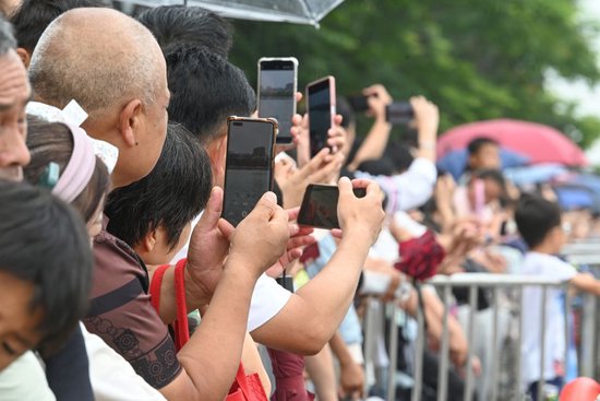 2026年6月19日，小区滨水步道边的观众举起手机，拍摄龙舟竞速。澎湃新闻记者 吴栋 图