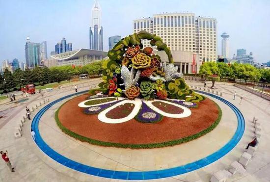 今年“五一”期间,人民广场喷水池区域搭建的巨型绿化艺术景观——“繁花似锦”,高约12米,以上海市花白玉兰等花卉为主要花型图案,并用了20万株各类时令春花及植物搭配点缀 图片来源:上海黄浦
