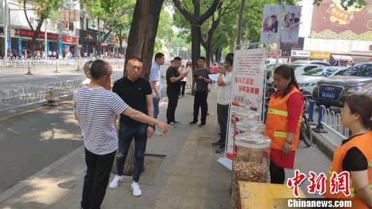 宣传现场用玻璃罐展示环卫工人每天清扫过程中收集到的烟头,并有环卫工人向路过的群众进行讲解。 冯嘉伟 摄