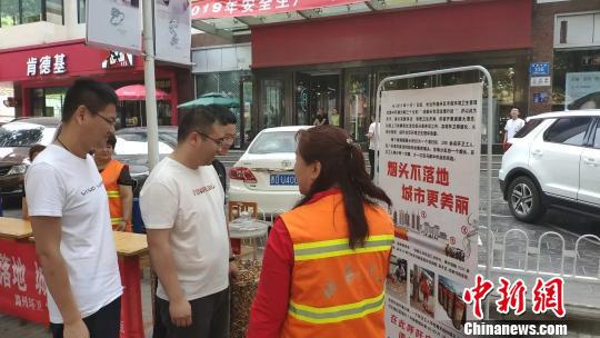 宣传现场用玻璃罐展示环卫工人每天清扫过程中收集到的烟头,并有环卫工人向路过的群众进行讲解。 冯嘉伟 摄