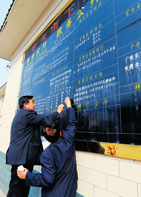 程厚福(左一)在村务公开栏上填写相关内容。