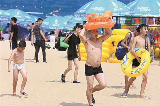 在大梅沙海滨公园，准备下海游泳的市民举着游泳圈遮挡烈日。