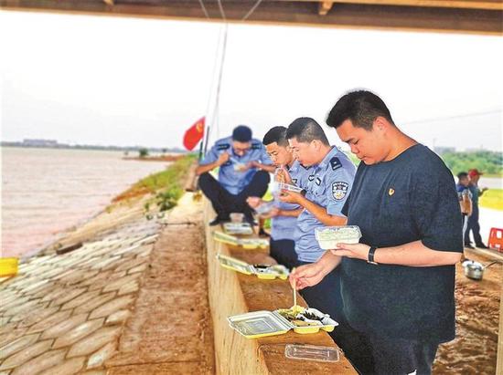 ▲杨小旭（右一）与当地民警利用抗洪抢险间隙在圩堤吃盒饭。受访者供图