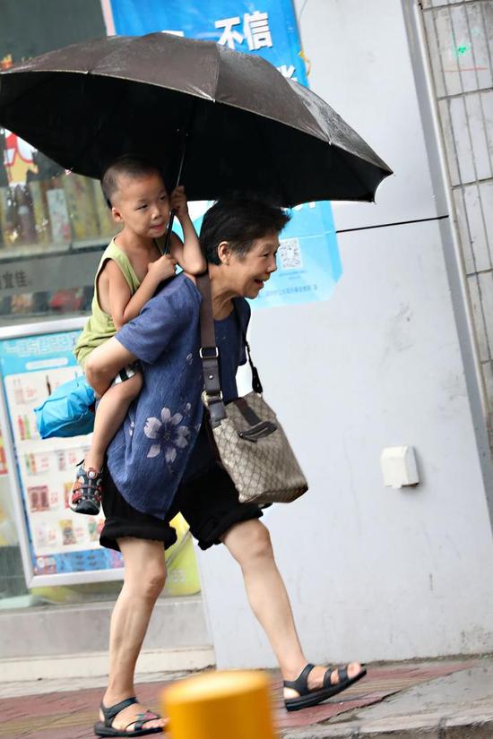 西环路上，奶奶背着孙子出行，孙子为奶奶打伞。