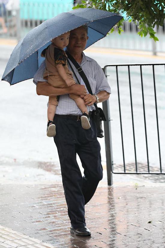 西环路上，爷爷为孙儿打伞。