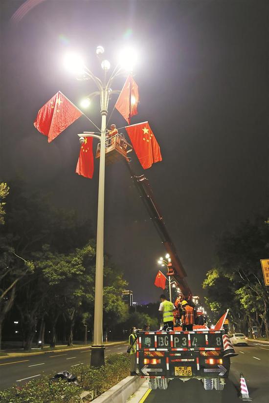利用深夜车辆较少的时间段，安装工人拿着国旗和张挂装置爬上安全梯，逐个将国旗安装到位。 深圳晚报记者 陈玉 摄