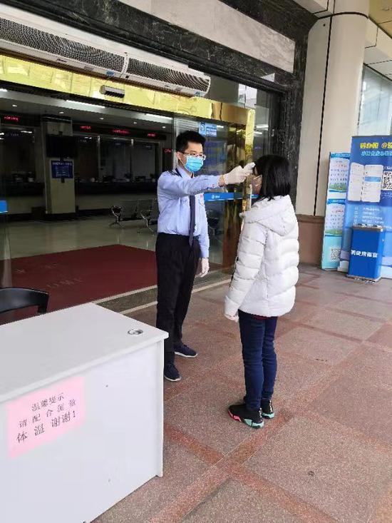 在国家税务总局深圳市龙华区税务局第一税务所(办税服务厅)门口,疫情防控志愿队成员陈思超正在为前来办税的纳税人测量体温。