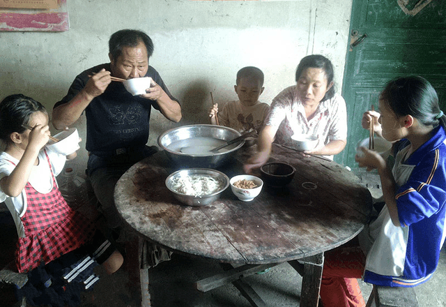 图上一家人正在吃饭,简单的一碗咸菜,一盆清水面条就是一家人的饭菜.