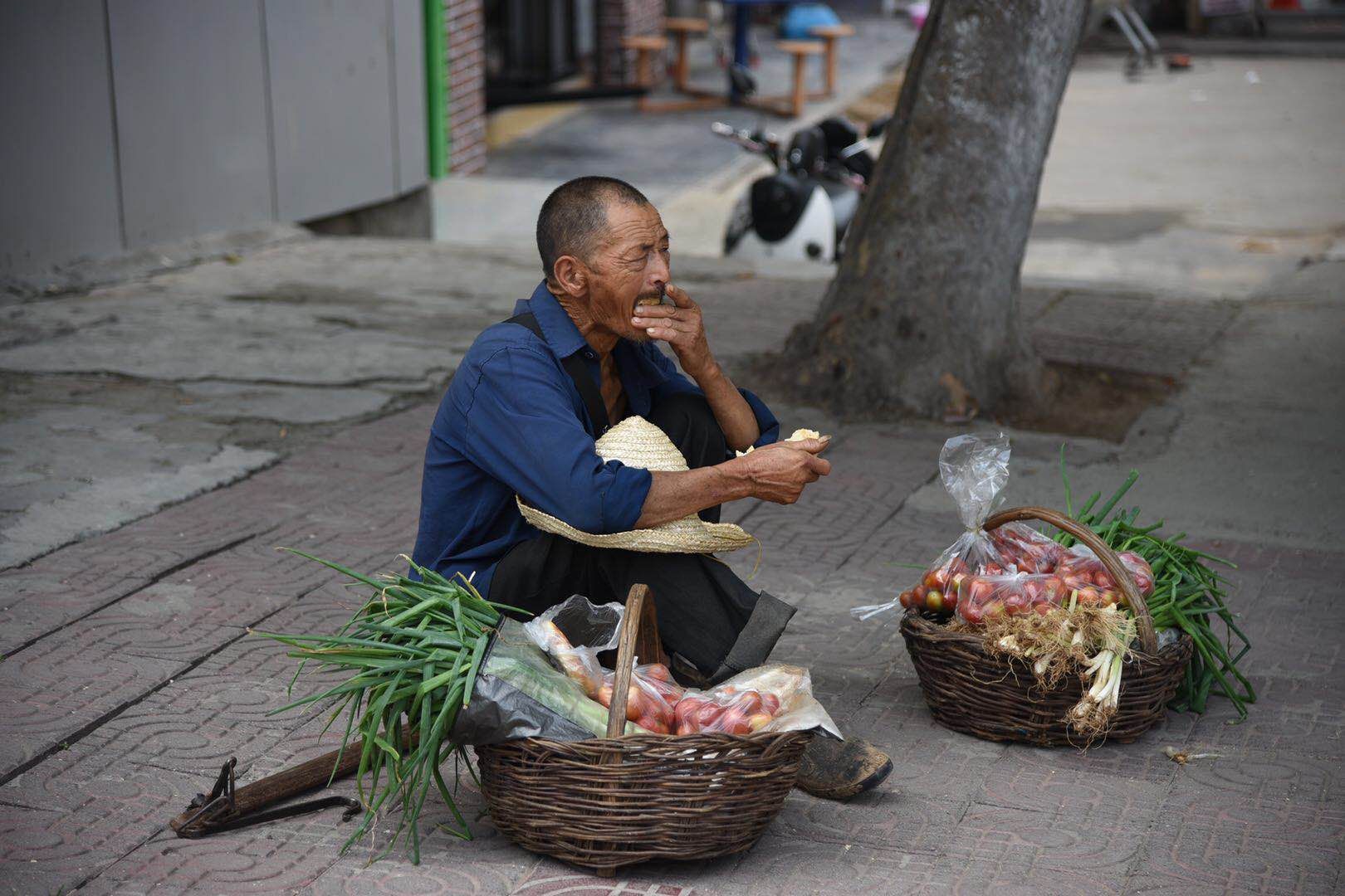 一根扁担,两只竹篮,这位在街头卖菜的老人,正在等待顾客