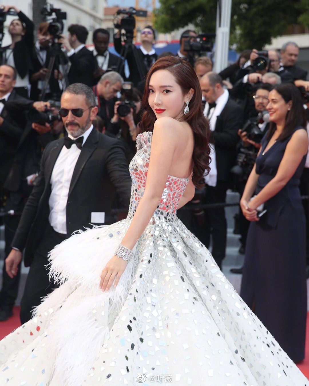 一头浪漫波浪长卷发，搭配精致妆容，身穿白色闪耀羽毛长裙