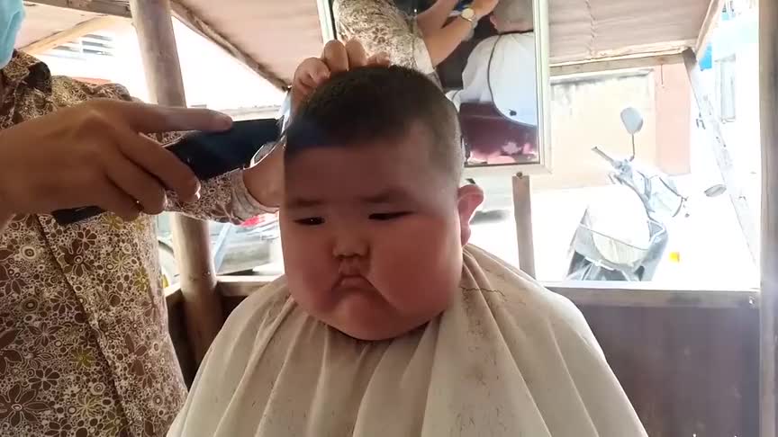 小胖子被爸爸抓来理发,小娃一脸不高兴,爸爸还一旁个